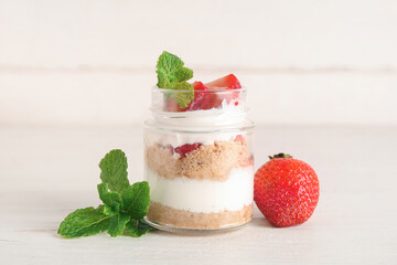 Jar with delicious strawberry cheesecake on white wooden background