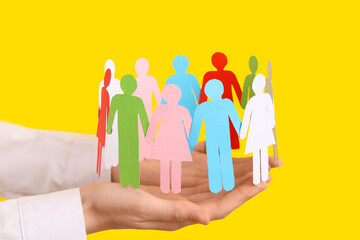 Female hands with paper human figures on yellow background, closeup. Diversity and inclusion concept