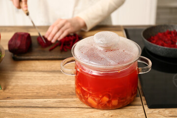 Young woman cutting beetroot for delicious borscht on wooden board in kitchen, closeup