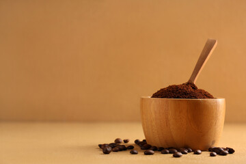 Wooden bowl of coffee powder with beans and scoop on beige background