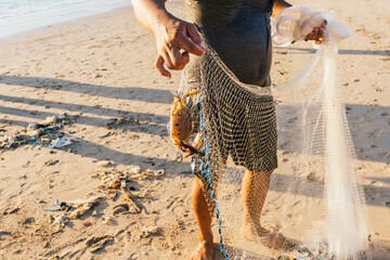 Fisherman holding net with captured crab on sandy beach