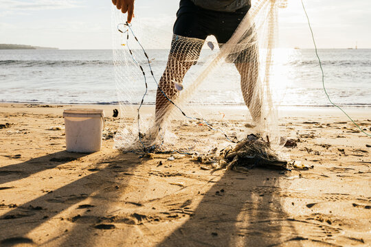 Fisherman collecting catch in net on sandy beach