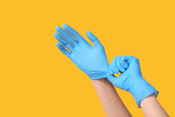 Female doctor putting medical gloves on her hands against yellow background