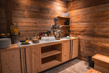 Cozy refreshment area with wooden walls, a polished samovar, cups, infused water, snacks, and warm lighting in an Italian Alps luxury hotel.