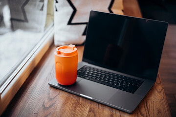 Laptop and thermos cup by a window, essentials for remote work
