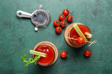Glasses of bloody mary cocktail with celery and tomatoes on green background