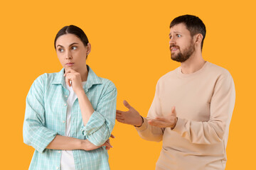 Young man trying to make peace with his wife after quarrel on yellow background