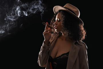 Sexy African-American woman smoking cigar on dark background