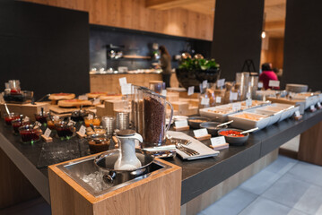 Breakfast buffet with cereals, fruits, pastries, and beverages on a sleek black countertop. Wood paneled interior and soft lighting create a warm ambiance.