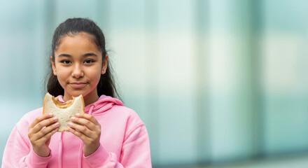 Hispanic young girl enjoying a sandwich in a pink hoodie outdoors