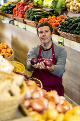 Adult man in apron sells onions in vegetables shop