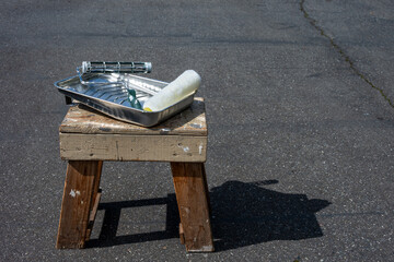 Obraz premium Home painting project, metal paint tray , roller handle and 3/8 inch nap roller sitting on an old paint stained wood stool 