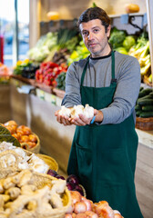 Man in supermarket seller in an apron carefully lays out fresh garlic on the shelves of the store