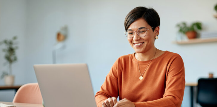 Asian young adult female working on laptop in casual home office setting