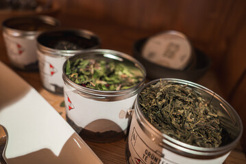 Open metal tins with green and herbal loose leaf teas on a wooden surface. Minimalistic labels and warm lighting create a rustic, cozy atmosphere.