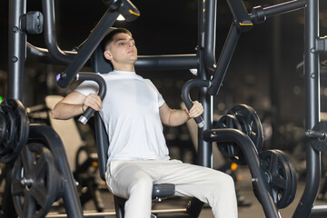 In gym, man uses chest press machine to strengthen arm muscles. Series of repetitions to consolidate result. Perseverance and persistence in achieving fitness goal. © JackF