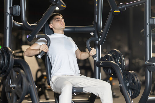 In gym, man uses chest press machine to strengthen arm muscles. Series of repetitions to consolidate result. Perseverance and persistence in achieving fitness goal.