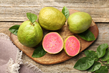 Fresh whole and cut guava fruits on wooden table, flat lay