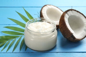 Organic coconut cooking oil in jar, halves of fruit and green branch on light blue wooden table,...