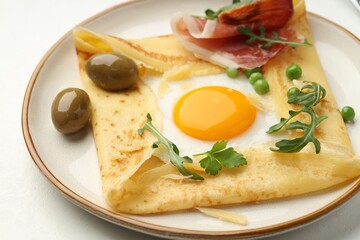 Delicious crepe with egg, bacon, olives and arugula on white table, closeup