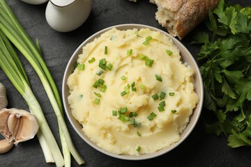 Delicious mashed potato with green onions served on black table, flat lay