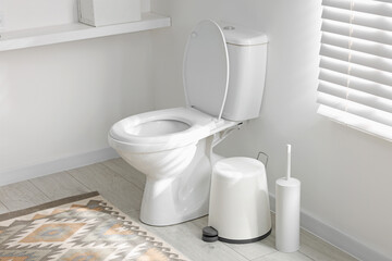 Toilet, brush and necessities near white wall in bathroom