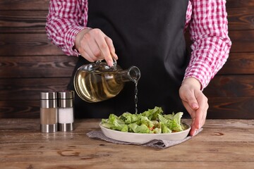 Woman pouring oil onto tasty salad at wooden table, closeup