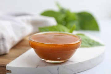 Tasty curry sauce in glass bowl and basil on white table, closeup