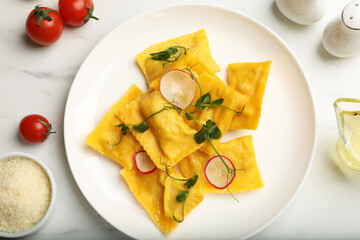 Delicious ravioli with microgreens, radish and other products on light table, flat lay