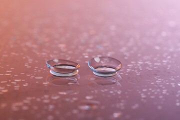 Pair of contact lenses and water drops on color gradient mirror surface, closeup