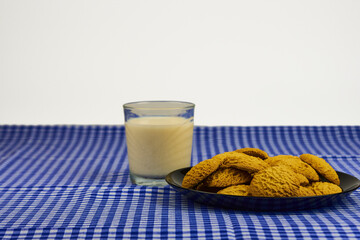 A plate of cookies sits on a blue and white checked tablecloth next to a glass of milk.