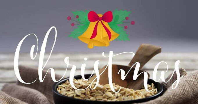 Christmas text and bell animation over bowl of oats with wooden spoon