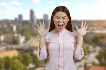 Screaming yelling young asian woman having nervous breakdown. Standing outdoors blurred cityscape background.