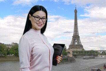 Young cheerful asian woman in glasses with tablet pc. Paris Eiffel Tower background.