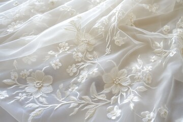 Obraz premium A close-up view of delicate Embroidered tulle lace fabric featuring floral patterns in soft white tones. The sheer material showcases intricate stitching and a light, airy texture.