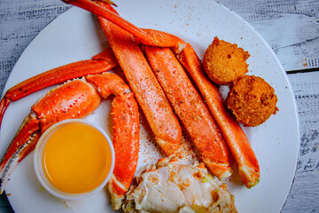 Top view of crab leg with hush puppies and and butter sauce in a white plate.