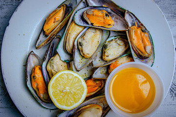 steamed mussels with slice of lemon and butter sauce in a white plate.