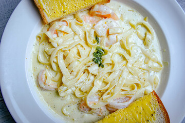 Top view of shrimp and pasta with white sauce served with slice of toast bread 