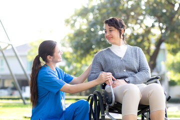 Young caucasian nurse comforting with patient while sitting on wheelchair in outdoor park, doctor...