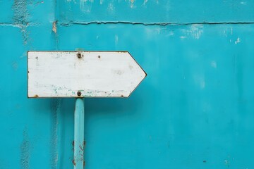 A weathered arrow sign pointing right on a teal painted wall