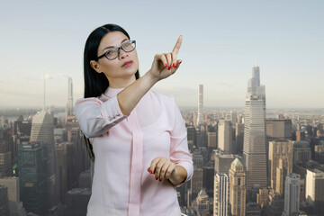 Asian businesswoman is pointing at copy space using invisible virtual screen. Urban cityscape...