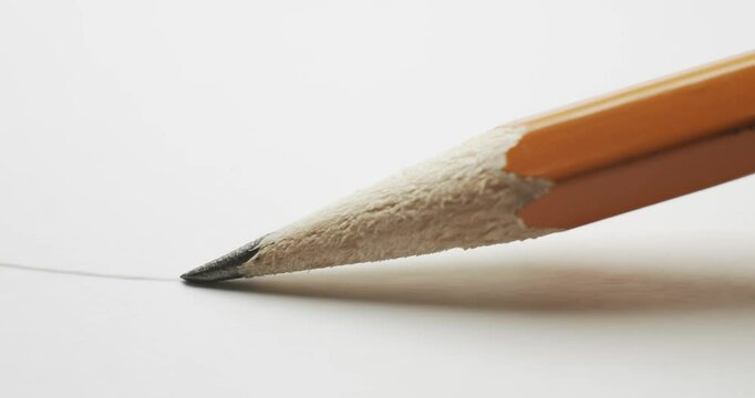 Yellow pencil with close up on sharp graphite pencil tip drawing a simple curvy line on plain white paper. Starting a pencil sketch with focus following the sharp lead writing a wavy doodle on paper.