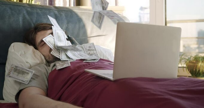 Man awakening from sleep by a flow of money flying from laptop. Man making money online while sleeping in bed. Earning money from comfort of bed. Lazy man passive income, easy money concept. Investing