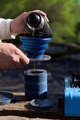 Outdoors coffee making process: an unrecognizable traveler pours hot water into a folding travel...
