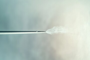 A metallic nozzle emits a plume of white vapor or smoke against a blurred background.