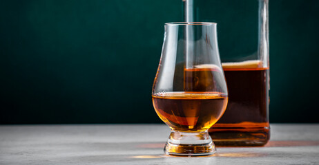 Single malt scotch whisky in glencairn glass with bottle on dark green background