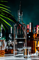 Vodka in glass and bottles of strong drinks on dark green background, hard light