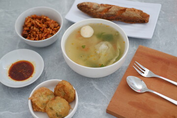 At the center is a bowl of clear soup containing vegetables, a fish ball, and possibly dumplings or cabbage.
