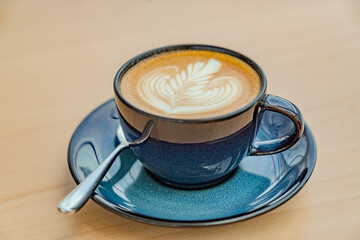 Photo of cappuccino coffee in blue ceramic cups with a spoon on a wooden table