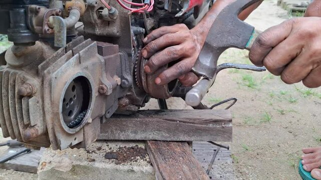 A mechanic's hand is trying to force open a component part of a motorbike's engine, using a large L-key and a hammer.